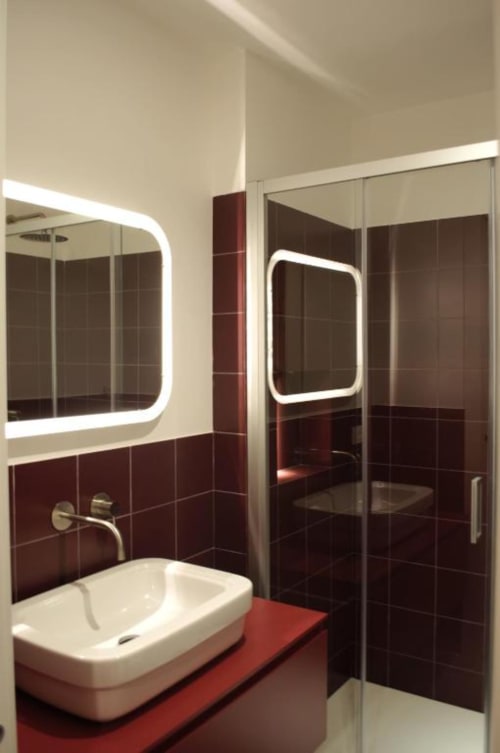Moderno bagno presso Le Dimore Del Duca Roma con piastrelle bordeaux, lavabo bianco, specchio LED e box doccia in vetro