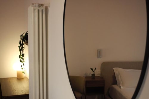 Camera accogliente a Le Dimore Del Duca Roma con radiatore bianco, comodino, specchio rotondo e illuminazione calda con vista sulla corte interna