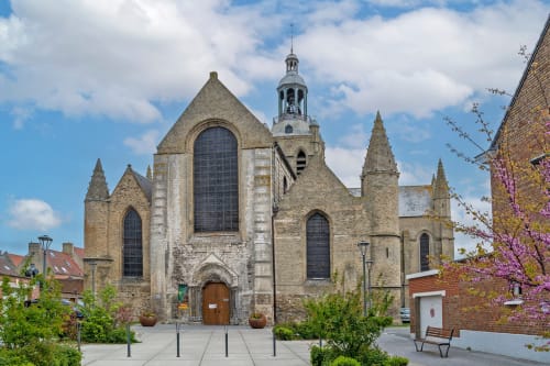 Historic stone church in Bourbourg, France, featuring Gothic architecture with tall spires and arched windows, near Cosyade
