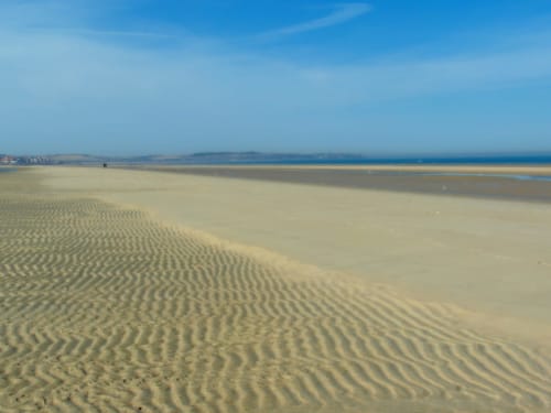Vast sandy beach with rippled patterns at Cosyade hotel, Bourbourg, France under clear blue sky