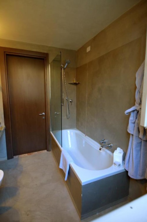 Modern bathroom at Hotel San Giovanni Resort in Saluzzo with white bathtub, glass shower enclosure, and beige tiled walls