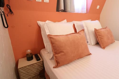Chambre moderne à la Villa Roseraie avec mur d'accent orange, literie blanche, coussins corail et table de nuit en bois à Vence.