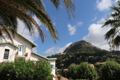 Vue de chambre de l'hôtel Villa Roseraie surplombant les palmiers, les montagnes et le paysage de Vence sous un ciel bleu
