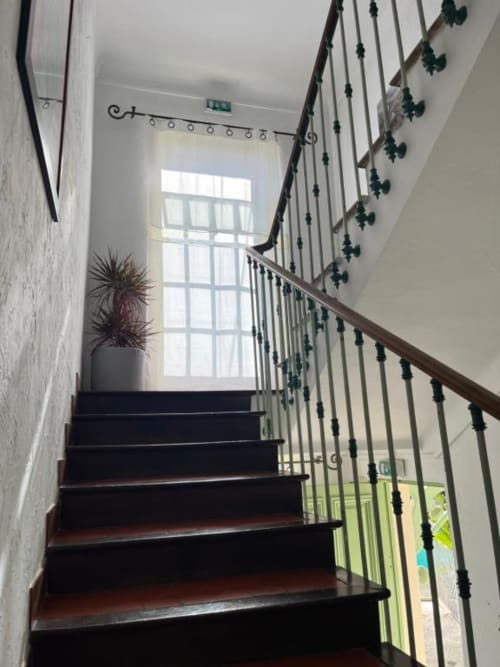Escalier aux marches en bois sombre et rampe métallique de l'Hôtel Villa Roseraie à Vence, menant à une sortie avec vue sur le jardin