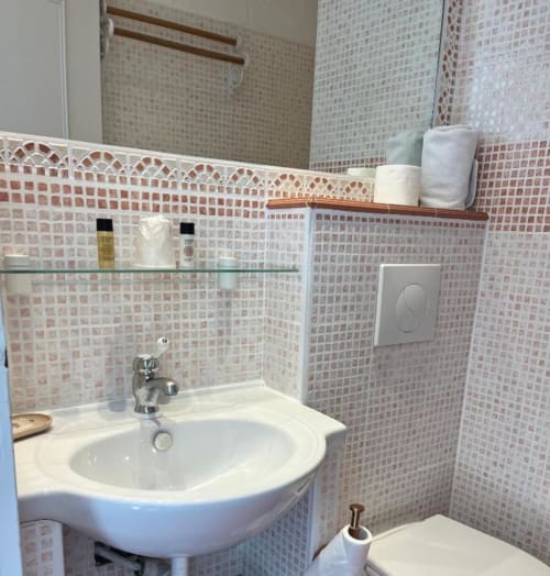 Salle de bain moderne de l'Hôtel Villa Roseraie à Vence avec carrelage mosaïque rose, lavabo blanc incurvé, miroir et papier toilette