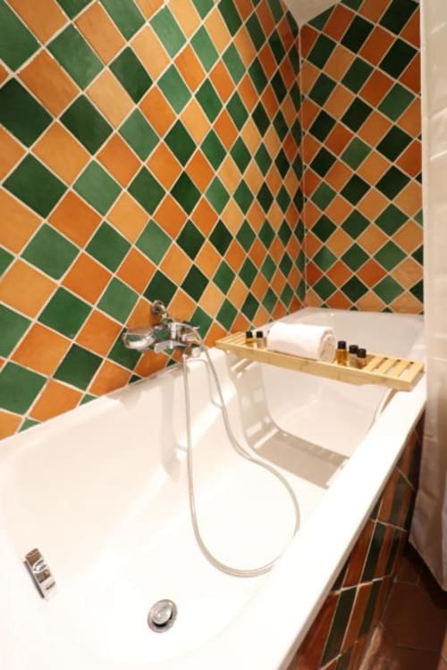 Salle de bain moderne de l'Hôtel Villa Roseraie avec carrelage aux motifs losanges colorés en vert et orange, baignoire blanche