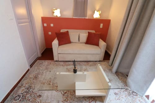 Suite de l'Hôtel Villa Roseraie à Vence : canapé crème avec coussins rouges, mur accent rouge et appliques modernes