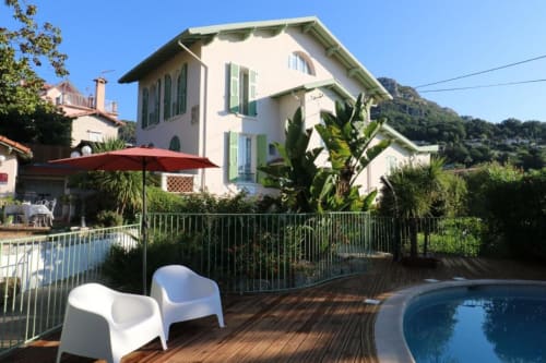 Villa Roseraie Vence hotel garden with pool, white chairs, red umbrella, and hillside views