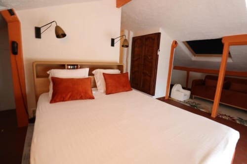 Chambre moderne à la Villa Roseraie avec lit queen, coussins rouges, touches orangées, mobilier en bois et accès à la vue montagne