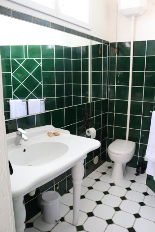 Bathroom at Hotel Villa Roseraie in Vence with green tiled walls, white pedestal sink, toilet, and black and white hexagonal