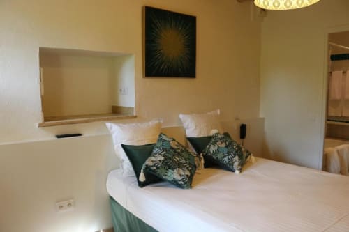 Chambre double à l'Hôtel Villa Roseraie Vence avec draps blancs, coussins de décoration et miroir au-dessus de la tête de lit