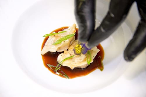 Elegantes ravioles presentados con salsa marrón y flores comestibles en Hotel San Giovanni Resort, Saluzzo