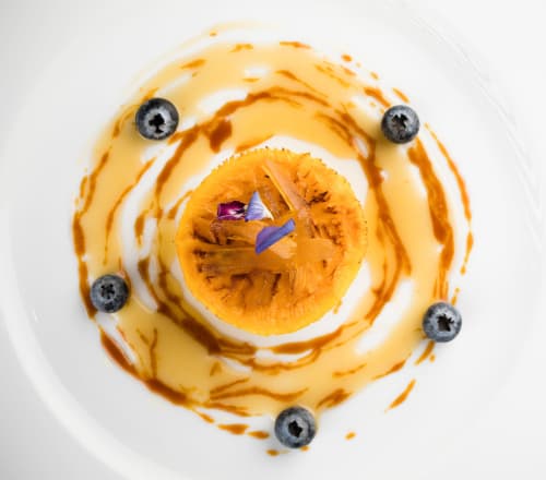 Sofisticado postre artístico con salsa naranja, rodaja de albaricoque, arándanos y flor púrpura del Hotel San Giovanni Resort