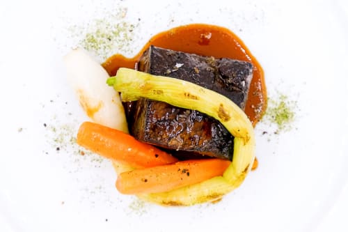 Plato gourmet presentado en Hotel San Giovanni Resort en Saluzzo, Italia con berenjenas asadas, zanahorias y salsa delicada