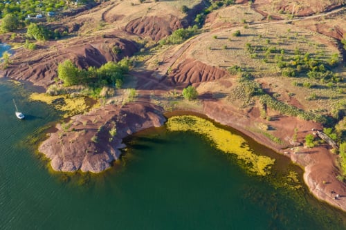 Vue aérienne de la campagne de Plaissan avec lac, formations rocheuses rouges et végétation verdoyante près de Chez Laure & Marc