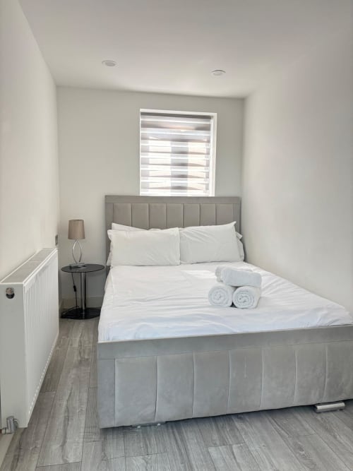 Modern bedroom with grey upholstered bed, white linens, and rolled towels at England Furnished Homes in High Wycombe