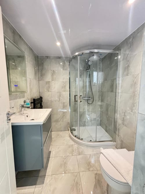 Modern bathroom in High Wycombe villa featuring marble tiled walls, curved glass shower enclosure, white sink with blue