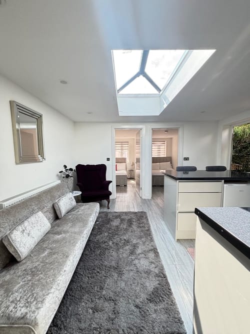 Modern open-plan living area at CozyNest villa in High Wycombe with skylight, grey sofa, kitchen, and garden views