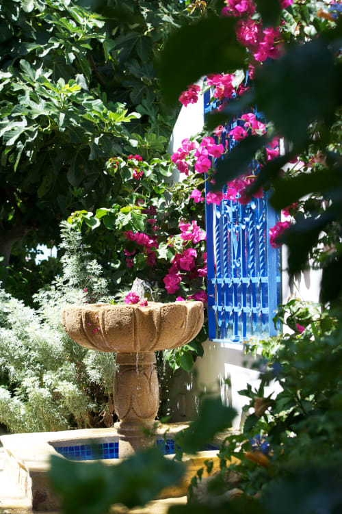 Buganvilla rosa vibrante cascada sobre una urna de piedra en el patio, puerta de madera azul visible en La Vista Medina Stays