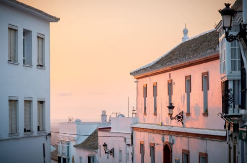 Atardecer en Medina Sidonia con edificios encalados y de tonos coral, arquitectura tradicional y faroles