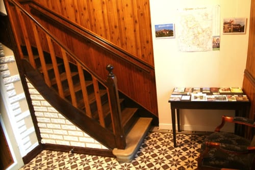 Wooden staircase in Les Gîtes de l'Impériale foyer, Sermizelles, with patterned tile floor, bulletin board, and pamphlets on