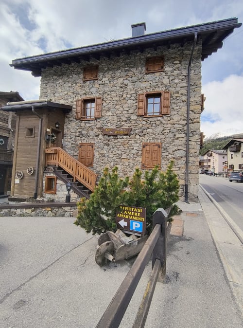 Edificio storico in pietra Al Dos a Livigno con vista montagna, persiane in legno, insegne per camere e parcheggio