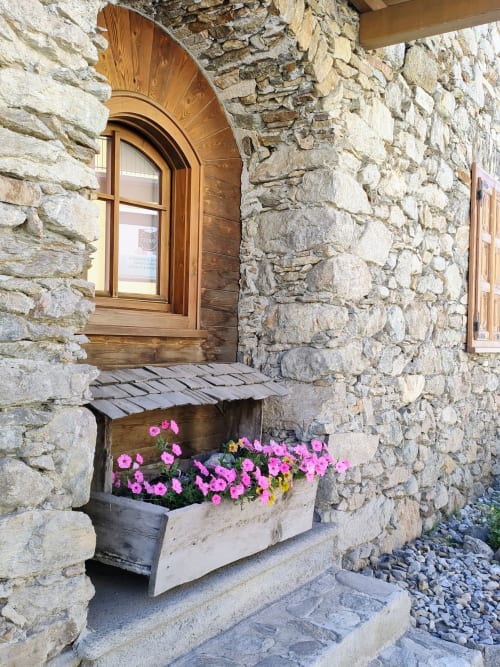 Ingresso con facciata in pietra dello studio Al Dos a Livigno, con porta ad arco in legno e fioriera rosa alla finestra