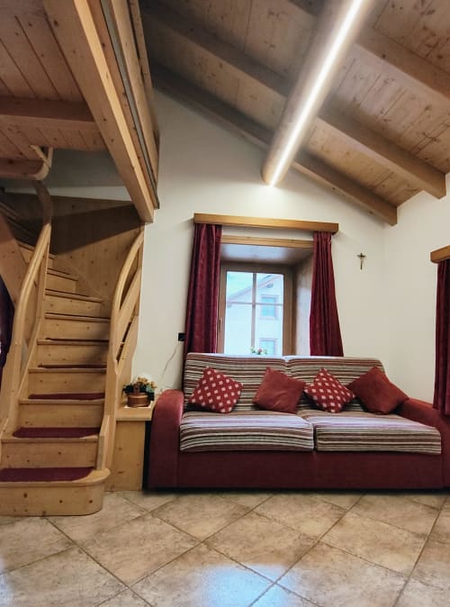 Monolocale ad Al Dos a Livigno con travi in legno, divano rigato, cuscini bordeaux e vista sulle montagne