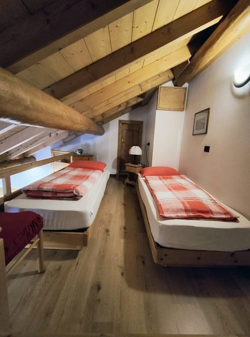 Accogliente monolocale in mansarda a Livigno con travi in legno, due letti singoli con biancheria rossa e vista sulle montagne