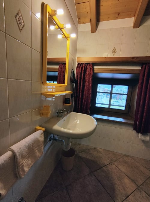 Bagno moderno con lavabo rotondo, specchio con cornice gialla e vista sulle montagne nell'appartamento Al Dos a Livigno