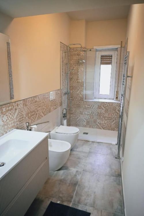 Bagno moderno nell'appartamento di Roma con sanitari bianchi, bidet, cabina doccia e dettagli in piastrelle decorative