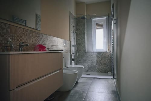 Bagno moderno in appartamento romano con toilette bianca, lavabo, doccia a filo e dettagli in mosaico