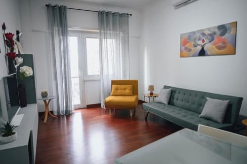 Soggiorno moderno a Roma con divano verde, poltrona gialla, pavimenti in legno e vista sulla città dal balcone