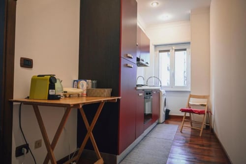 Cucina moderna di appartamento romano con armadi rossi, tavolo in legno, macchinetta da caffè gialla e sedia da pranzo vicino alla finestra