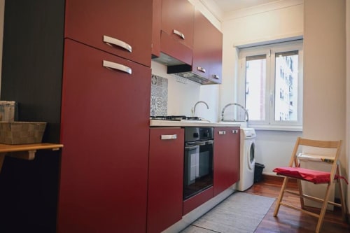 Cucina moderna rossa con elettrodomestici in acciaio inossidabile, lavatrice e sedia in legno nell'appartamento romano