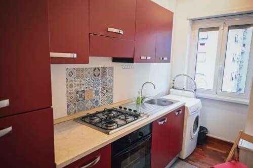 Cucina moderna con mobili rossi, fornello a gas, lavello, lavatrice e piastrelle decorative a Roma