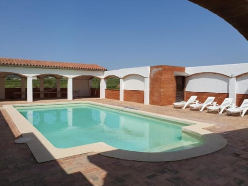 Turquoise swimming pool at Masia Rural Ca l'Eloi Janet villa near Barcelona, with lounge chairs and red brick buildings