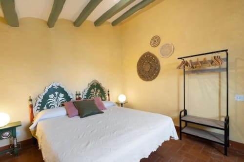 Dormitorio rústico en Masia Rural Ca l'Eloi Janet con paredes amarillas, cabecero decorado en verde, ropa de cama blanca y techo de madera