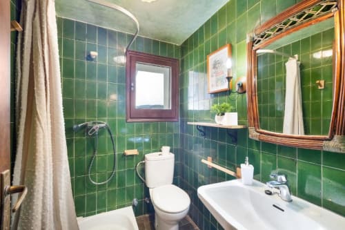Bright green tiled bathroom at Masia Rural Ca l'Eloi Janet villa near Barcelona, with white fixtures and wooden-framed mirror