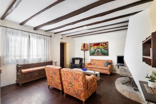 Sala de estar rústica en Masía Rural Ca l'Eloi Janet cerca de Barcelona con vigas de madera, sillones estampados y decoración tradicional
