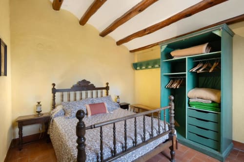 Dormitorio rústico en Masia Rural Ca l'Eloi Janet, Barcelona, con vigas de madera expuestas, cama de hierro y armario turquesa.