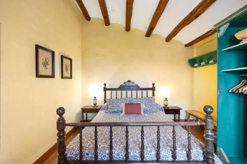 Dormitorio rústico en Masía Rural Ca l'Eloi Janet con vigas de madera, cama de hierro y estantería turquesa cerca de Barcelona