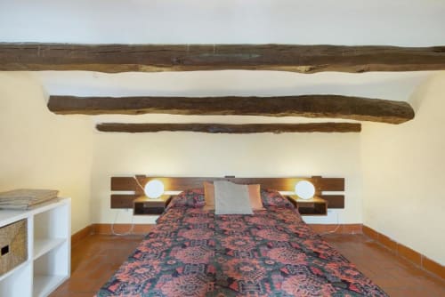 Rustic bedroom at Masia Rural Ca l'Eloi Janet near Barcelona with exposed wooden beams, patterned bedspread, and built-in