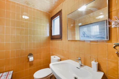 Bathroom with orange tile walls, white sink, toilet, and mirror at Masia Rural Ca l'Eloi Janet villa near Barcelona