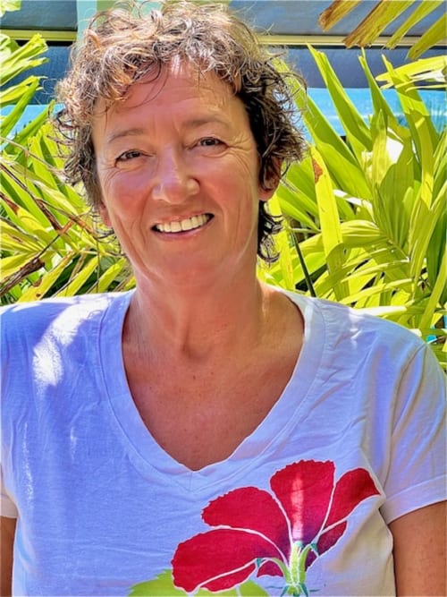 Donna sorridente a Chez Marie et Philippe a Marie-Galante che indossa una camicia lavanda con disegno di fiore rosso