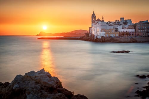 Atardecer sobre pueblo costero mediterráneo con arquitectura histórica y aguas tranquilas cerca de Barcelona