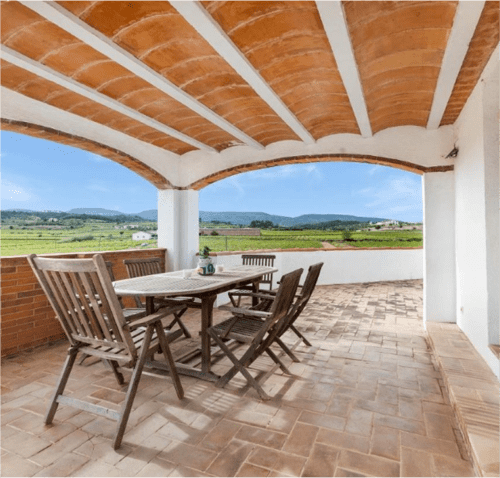 Terraza sombreada con vigas de madera que domina campos verdes en Masia Rural Ca l'Eloi Janet, retiro rural en la comarca de Barcelona