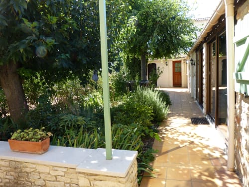 Villa Thébaïde courtyard with terracotta pot, lush greenery, stone building and covered walkway in Laudun L'Ardoise