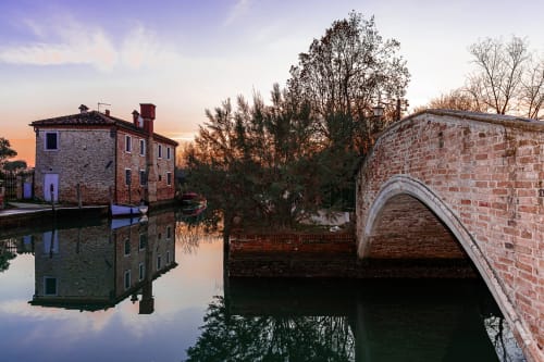 Casanova Hideaway BnB a Venezia: edifici storici in mattoni riflessi nell'acqua calma al tramonto con ponte ad arco