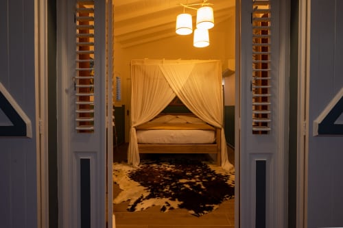 Lit à baldaquin élégant avec rideaux crème à la maison d'hôtes Aïchi chez Marie et Philippe, Marie-Galante, avec éclairage chaleureux